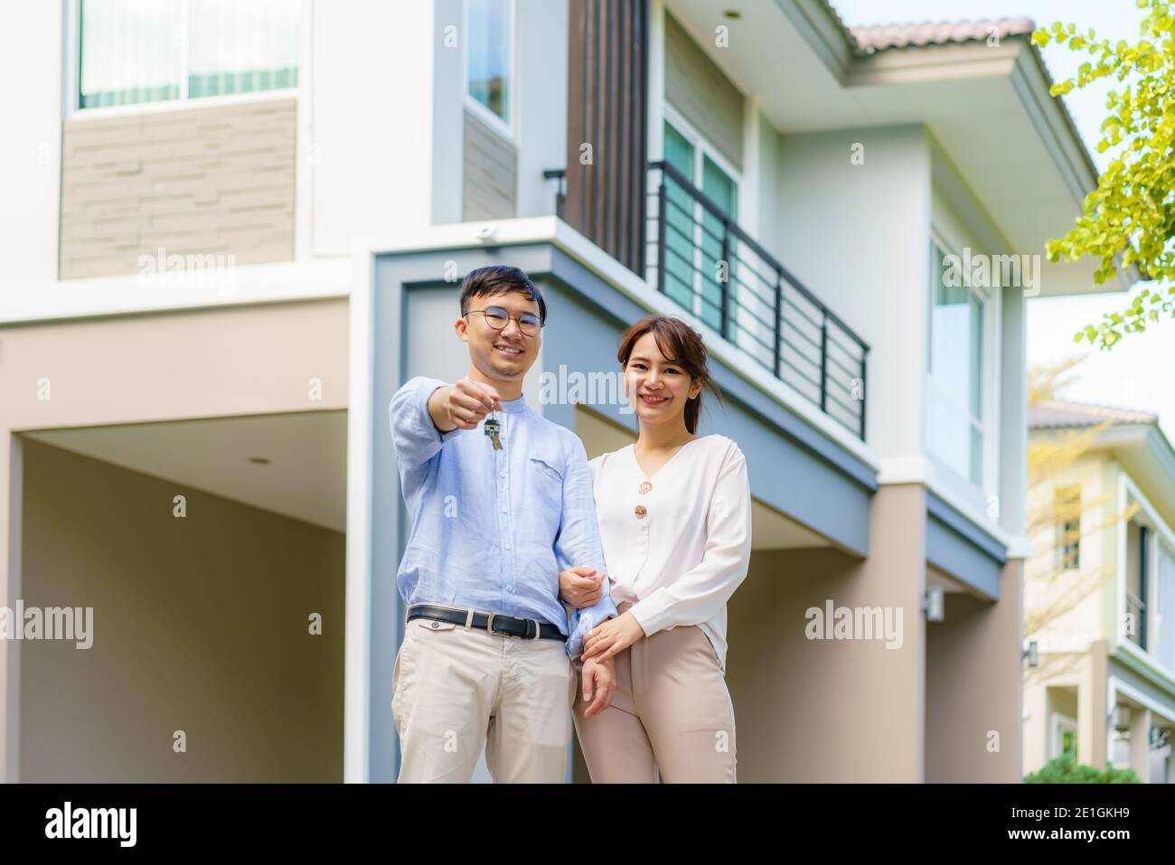 Porträt des jungen asiatischen Paares, das zusammen steht und umarmt und die Haustaste hält, die vor ihrem neuen Haus glücklich aussieht, um neues Leben zu beginnen. Familie Stockfoto