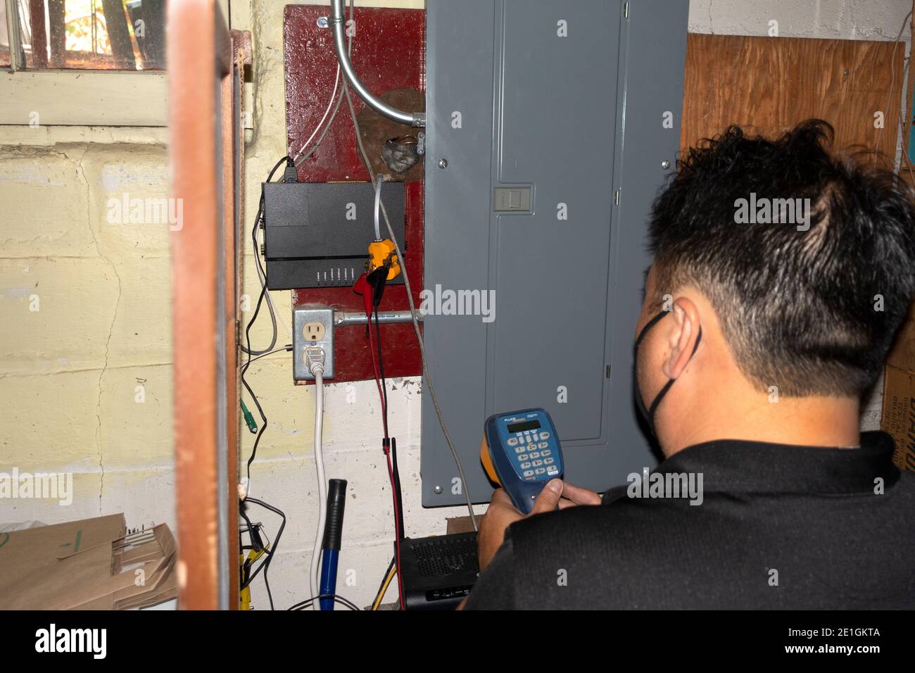Maskierter Century Link-Arbeiter im Keller, der eine Reparatur an der Internet-Leitung mit einem digitalen Instrument macht. St. Paul Minnesota, USA Stockfoto