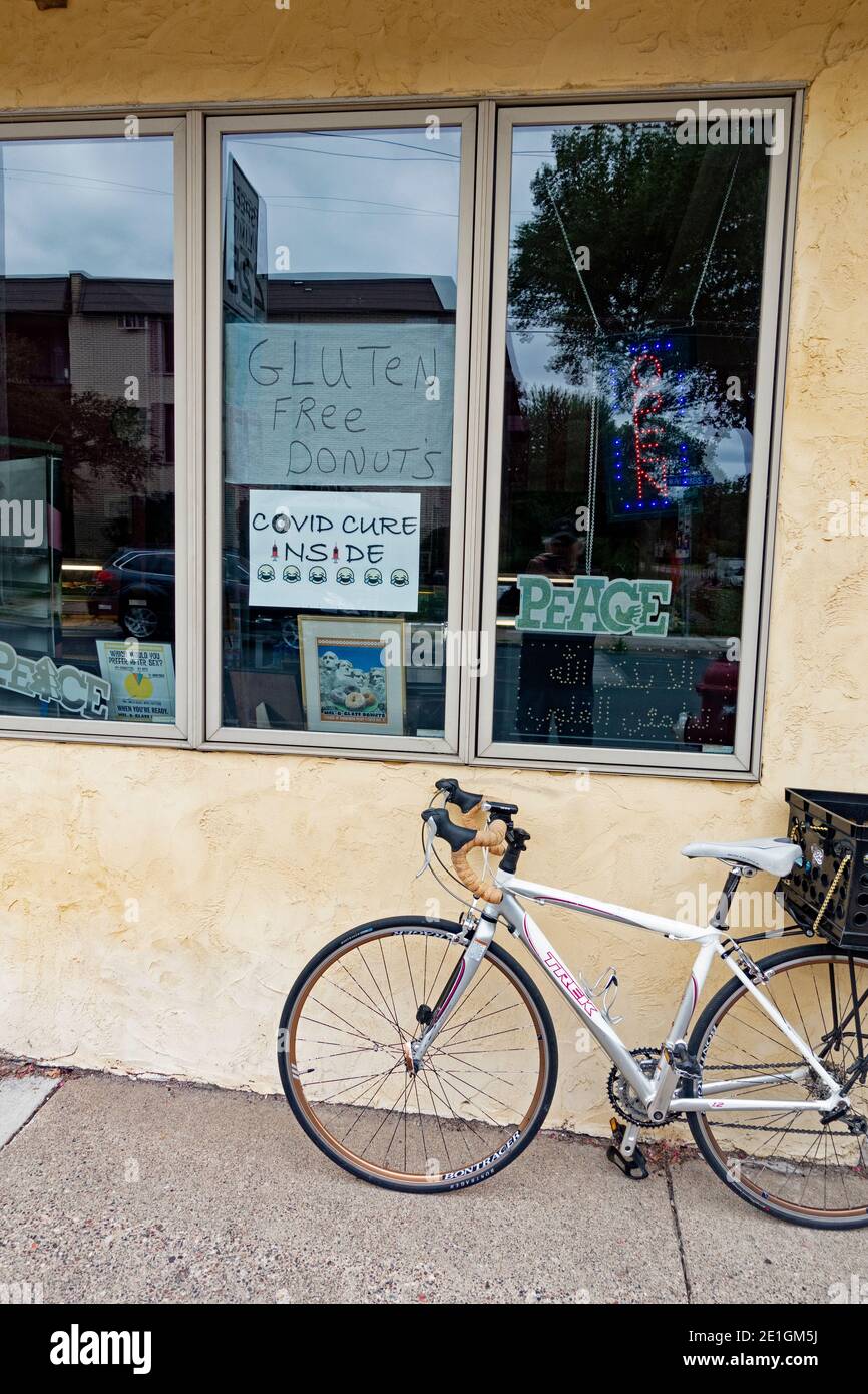 Fahrrad am Fenster in der Bäckerei Mel-O-Glaze mit Fensterschildern für eine Covid-Kur und glutenfreien Donuts geparkt. Minneapolis Minnesota, USA Stockfoto