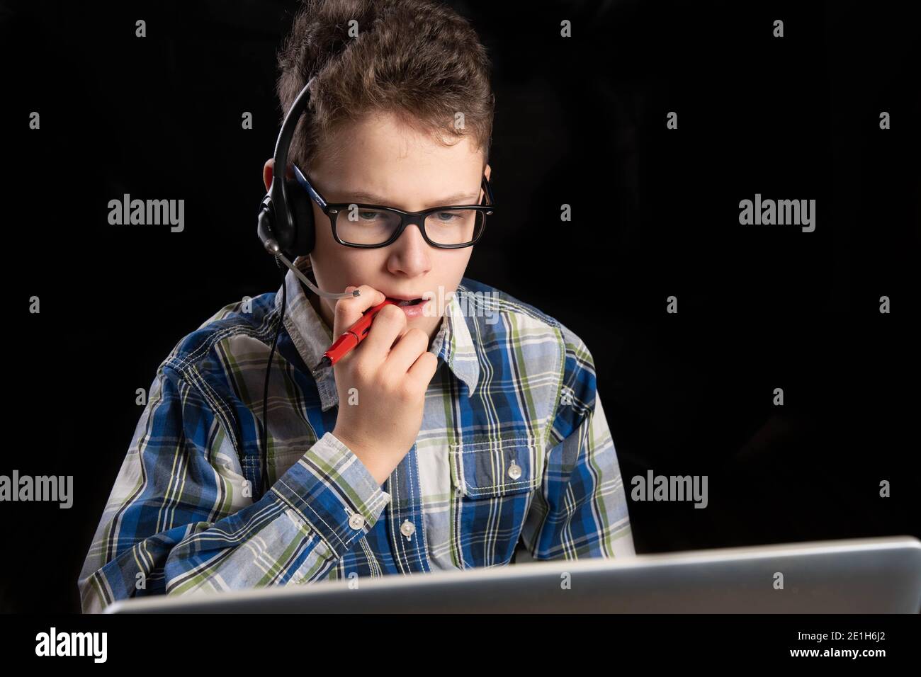 Junge mit Brille und Hemd und Mundmaske mit Headset Stift im Mund grübeln Stockfoto