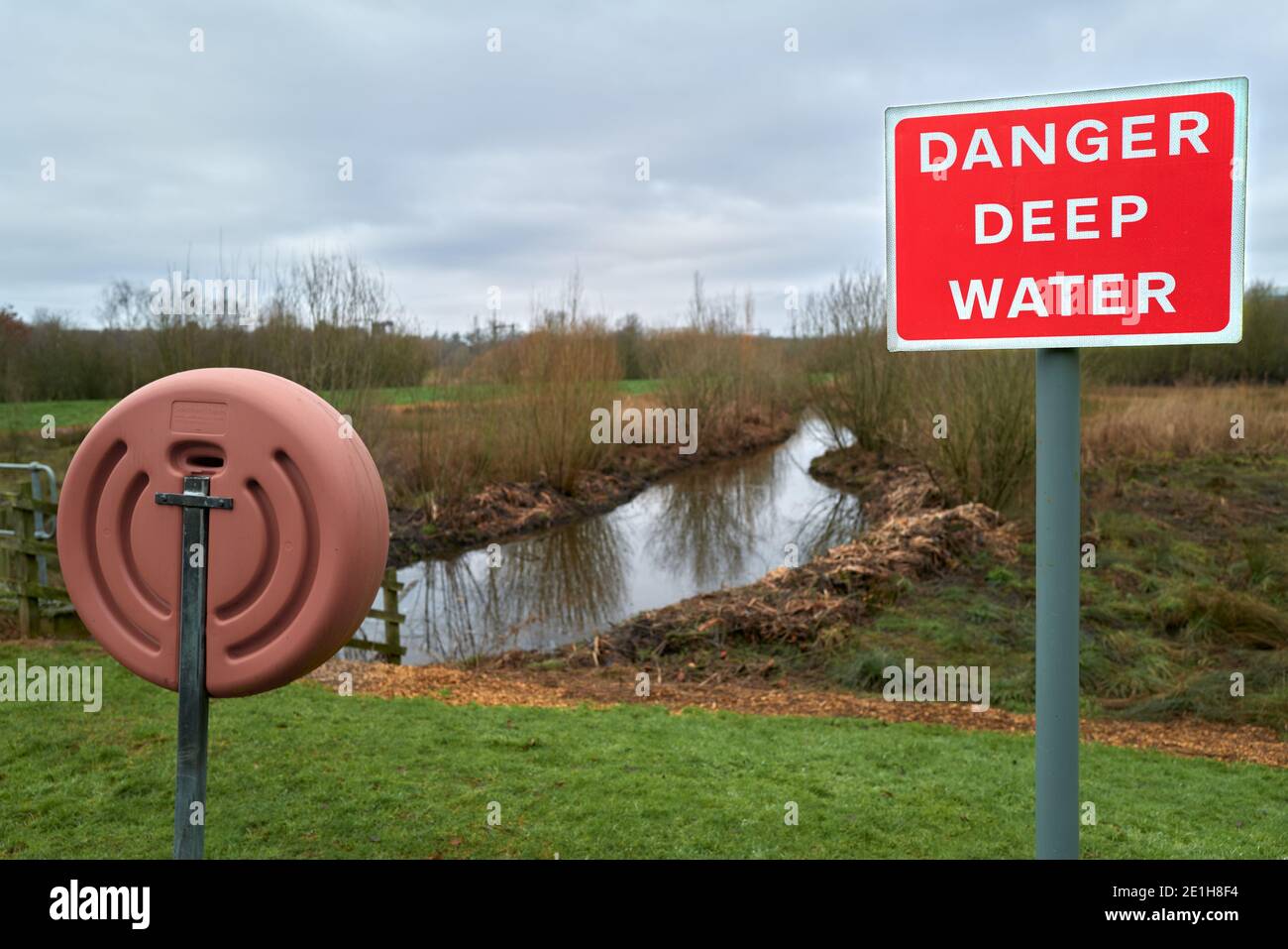 'Danger Deep Water'-Hinweis neben einer Rettungsboje auf unbebautem Land in Kettering, Nhants, England. Stockfoto