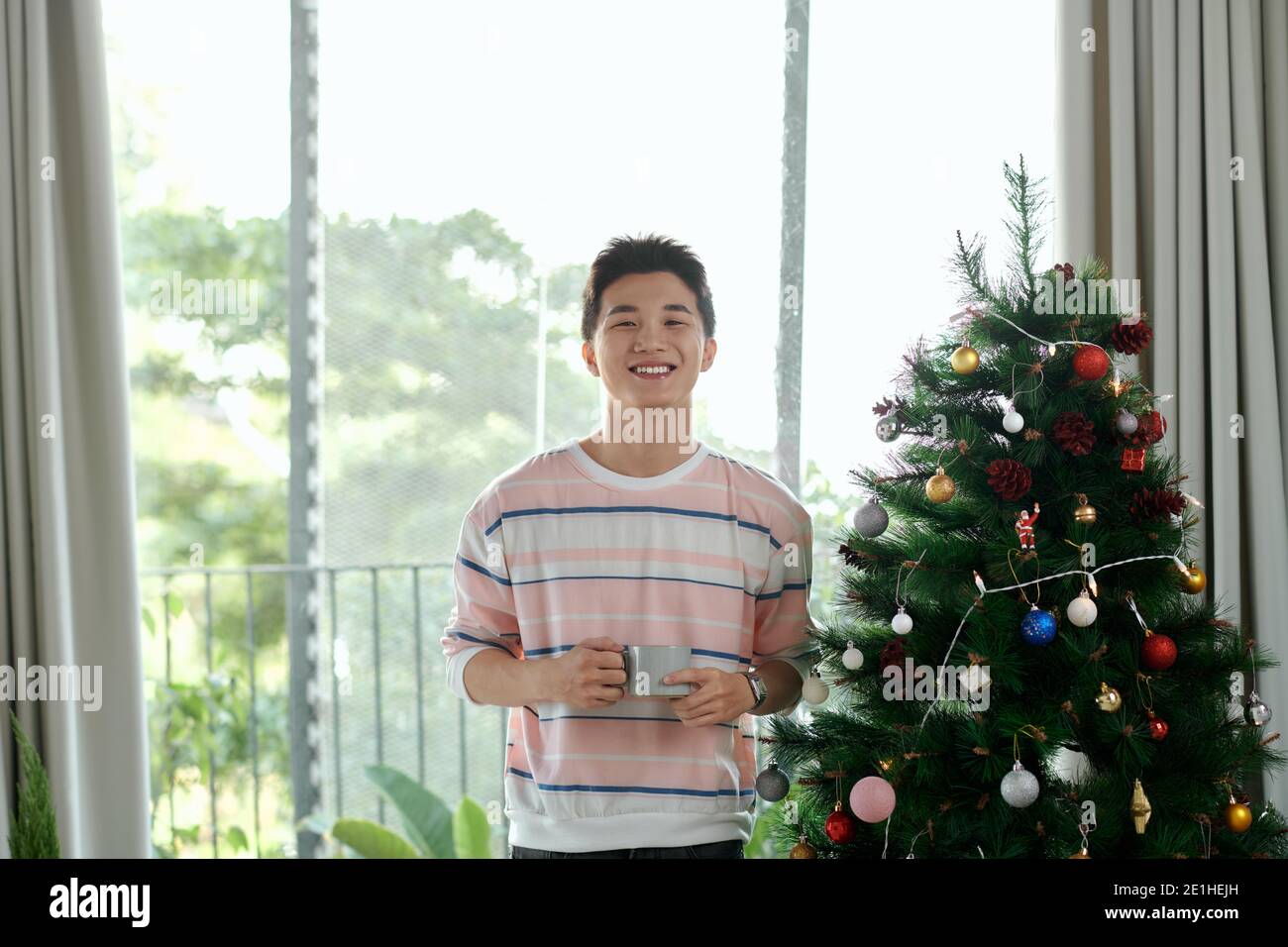 Eleganter Mann mit positiver emotionaler Gesichts posiert mit Tasse Kaffee mit weihnachtsbaum und Neujahr Dekorationen Stockfoto