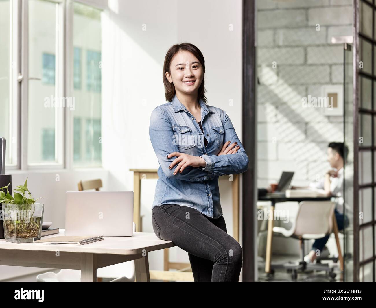 Porträt einer jungen asiatischen Geschäftsfrau, die in die Kamera schaut Lächelnde Arme gekreuzt Stockfoto