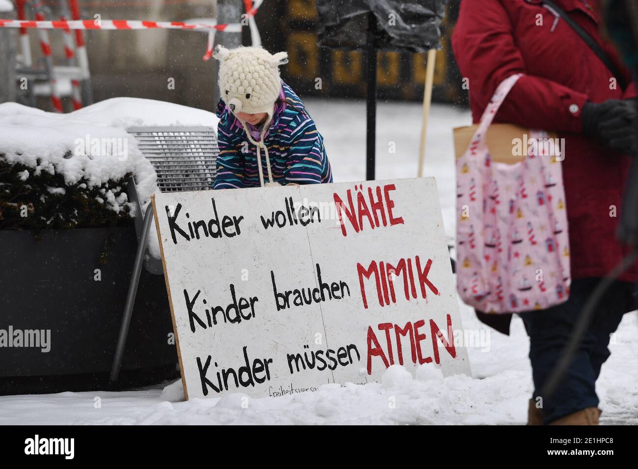 Freiheitsversammlung am 6. Januar 2021: Aussperrung gegen Kinderrechte und Menschenwürde auf dem Marienplatz in München. Ein Kind spielt hinter einem Zeichen: KINDER WOLLEN NAHE SEIN, Kinder BRAUCHEN MIME, Kinder MÜSSEN ATMEN. Demonstration versus Schließung von Schulen und Kindertagesstätten. Weltweite Nutzung Stockfoto