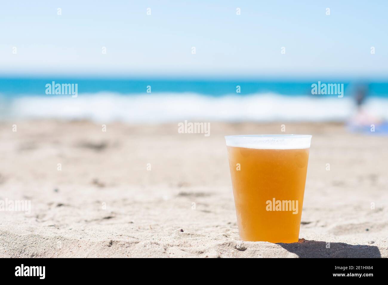 Plastikglas mit kaltem Bier auf dem Strandsand Stockfoto