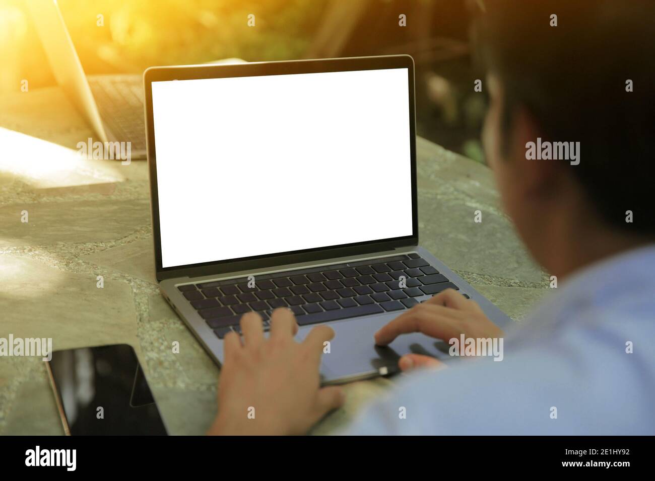 Zugeschnittenes Bild eines jungen Mannes, der in einem Garten an seinem Laptop arbeitet, Rückansicht der Hände eines Geschäftsmanns, der am Büroschreibtisch mit dem Laptop beschäftigt ist und auf Computern tippt Stockfoto