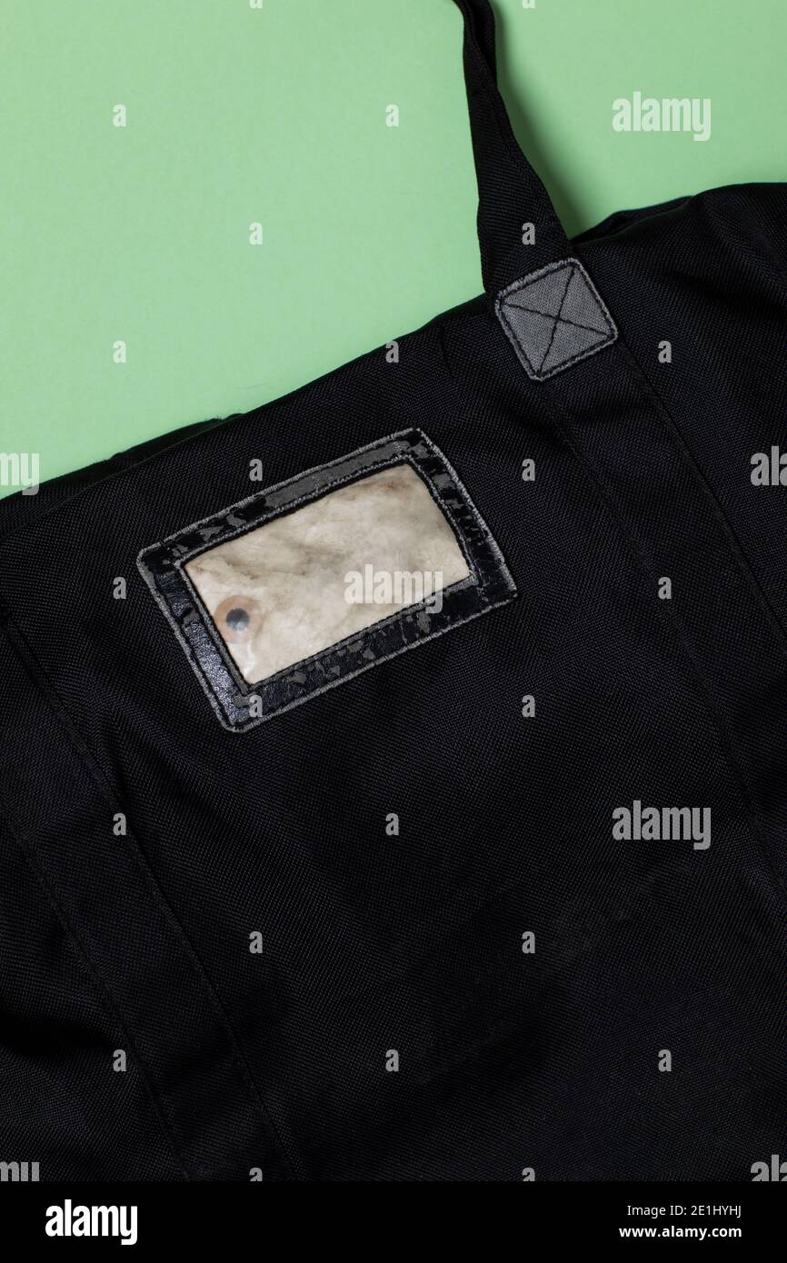 Eine schwarze alte Tasche mit einem alten Etikett auf der Tasche genäht. Leerer Raum. Vertikale flache Lage Schuss auf einem grünen Hintergrund Stockfoto