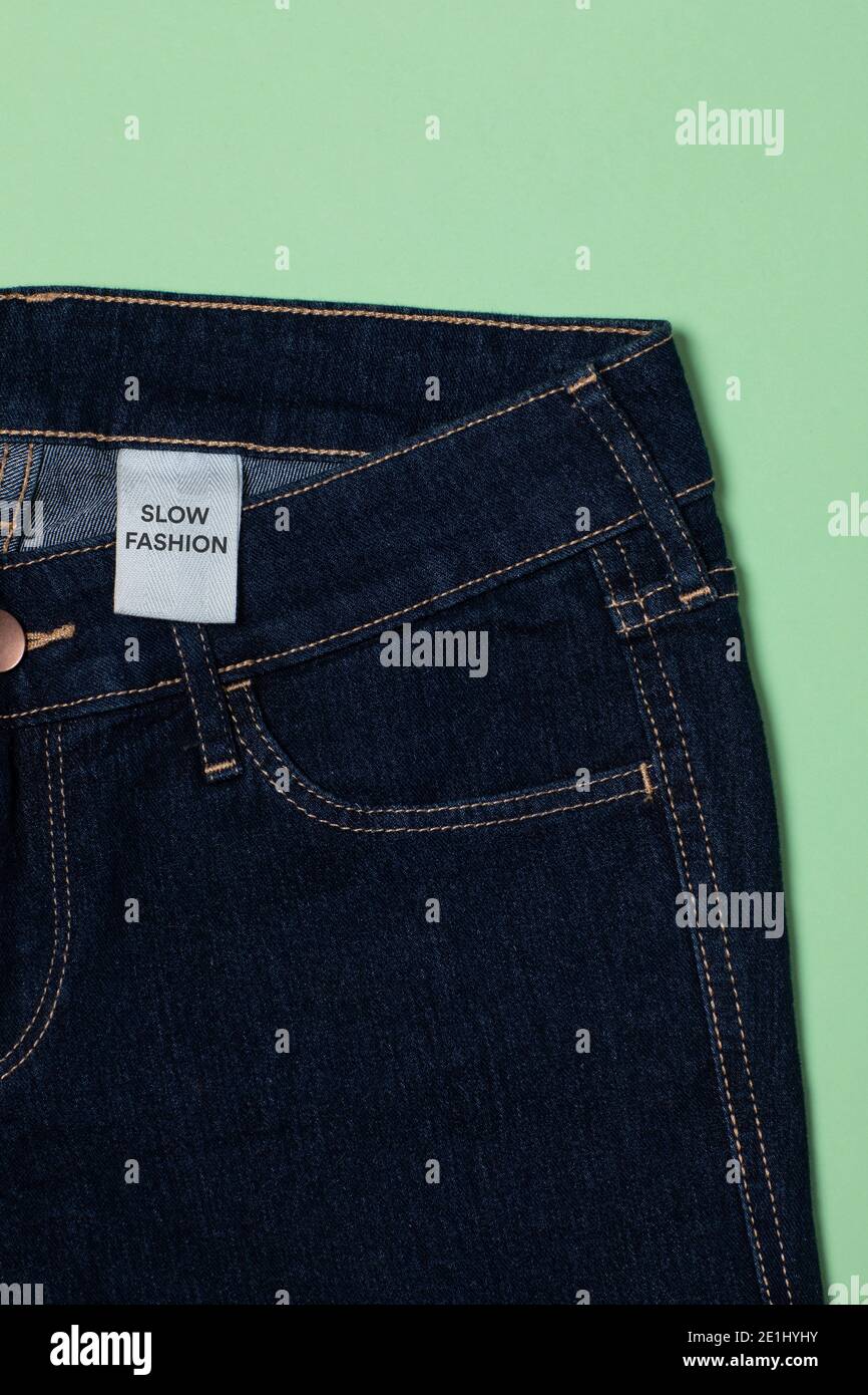 Blaue Jeans mit einem Kleidungsstück, das Slow Fashion sagt. Kreislaufwirtschaftsprinzip, Zero Waste Konzept. Handgemachte Kleidung und Verringerung der Abfälle in der Mode. De Stockfoto