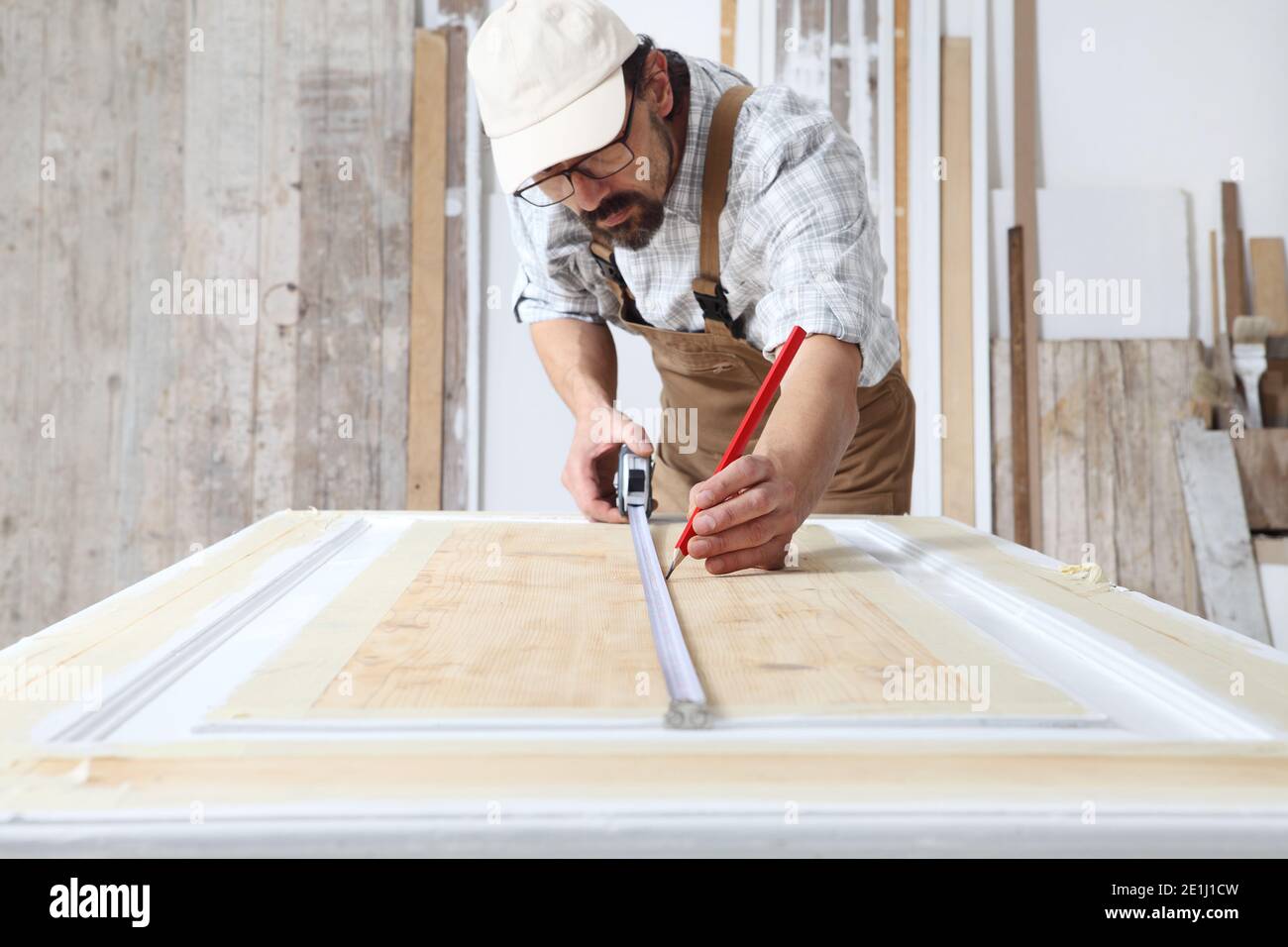 Zimmermann arbeitet das Holz in der Schreinerei Werkstatt, Maßnahmen auf Holztür mit einem Mesure-Band und einem Bleistift, tragen insgesamt Stockfoto