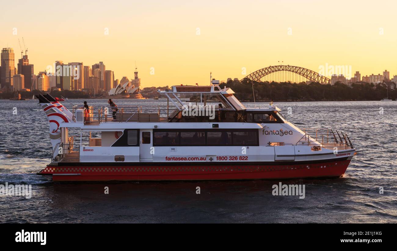 Ein Ausflugsboot auf dem Sydney Harbour, Australien, bei Sonnenuntergang, mit dem Sydney Opera House und der Harbour Bridge im Hintergrund Stockfoto