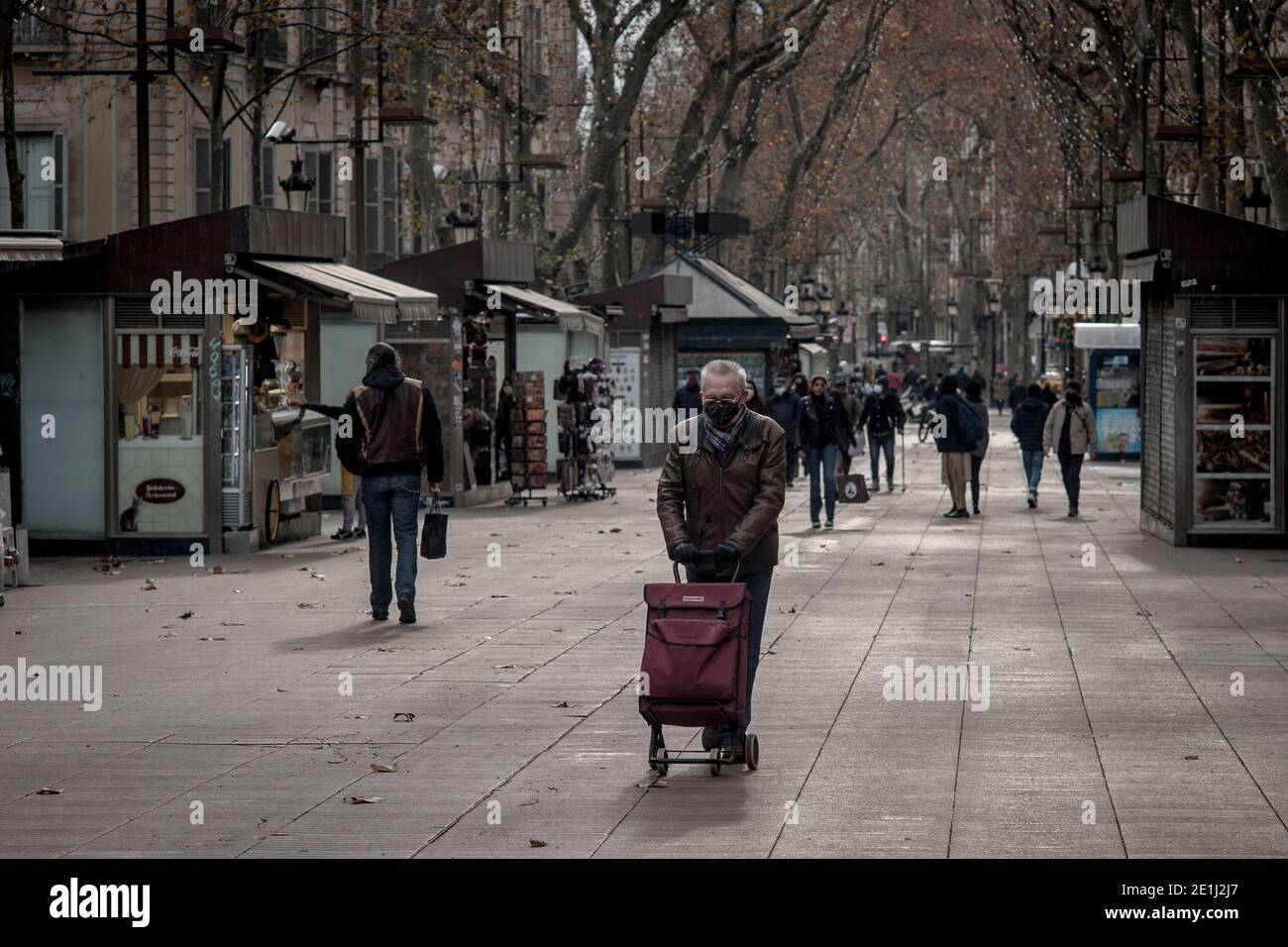 Ein Mann mit Gesichtsmaske schiebt den Einkaufswagen entlang der Rambla in Barcelona. Am Ende der Weihnachtszeit haben mehrere Regionen in Spanien die Maßnahmen verschärft, um die Ausbreitung des Coronavirus 3. Welle zu stoppen, da der Druck in Krankenhäusern steigt. Einige Studien kommen zu dem Schluss, dass der neue Coronavirus-Stamm, der erstmals im Vereinigten Königreich nachgewiesen wurde, seit zwei Wochen in Spanien im Umlauf ist. Stockfoto