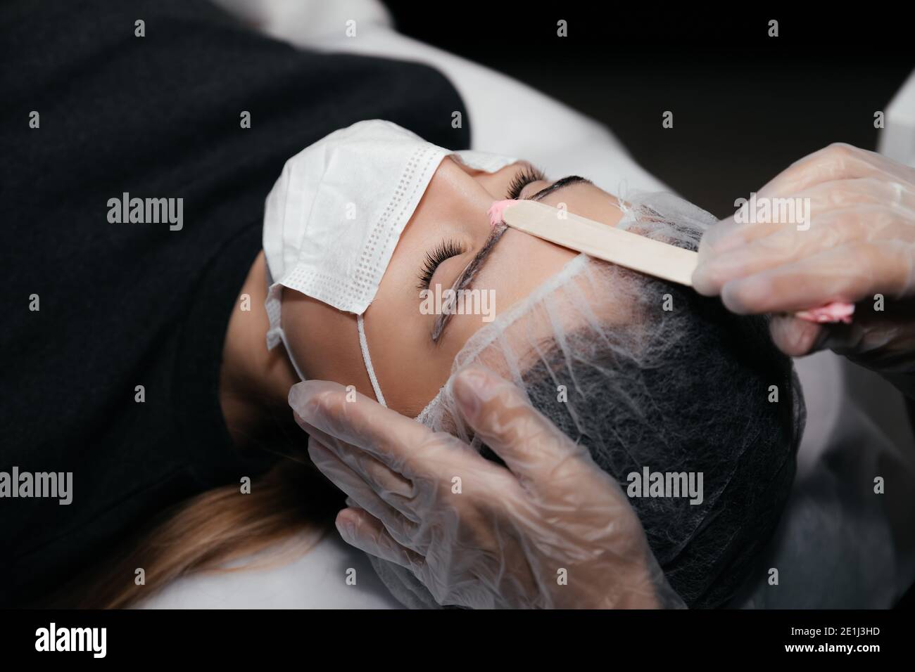 Gesichtshaarentfernung Verfahren durch heißes Wachs auf Holzstab,  Vorbereitung vor Permanent Make-up Tattoo auf Augenbrauen. Sicheres  Verfahren mit medizinischen Masken A Stockfotografie - Alamy