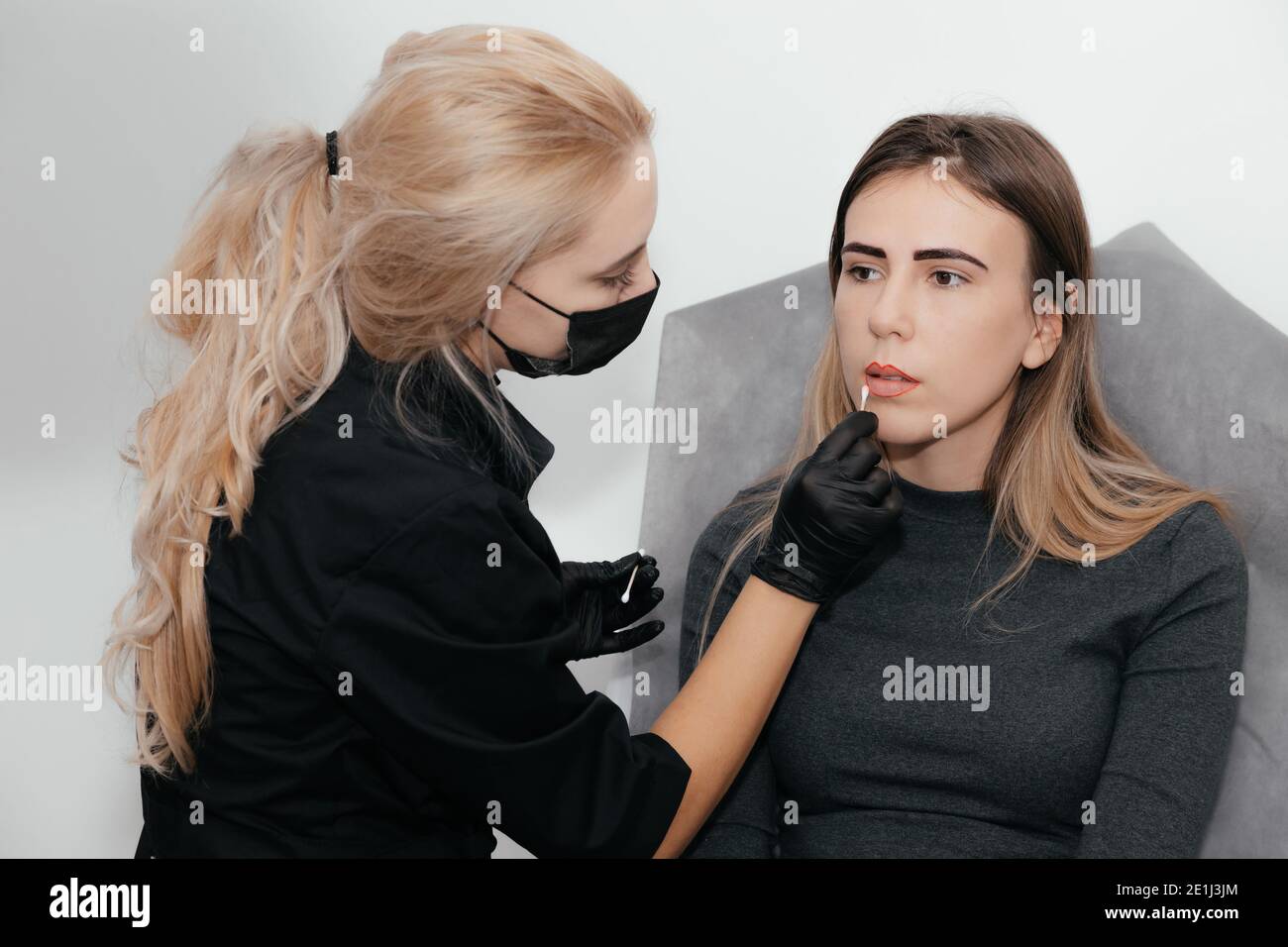 Permanent Make-up Master in medizinische Maske macht Lippen vor Form Permanente Make-up-Verfahren im Kosmetiksalon und korrigiert die Form mit einer Baumwolle Stockfoto