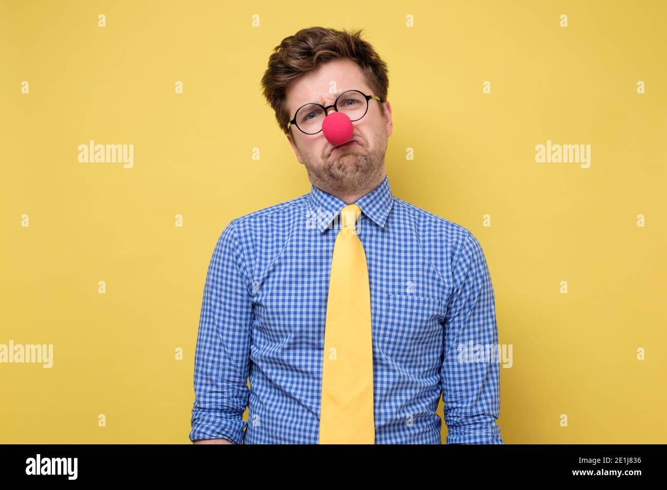 Trauriger kaukasischer Mann mit roter Clown-Nase an der gelben Wand. Er ist aufgebracht, dass niemand zu seiner Partei kam. Stockfoto