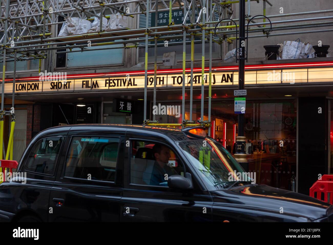 Schwarzes Taxi, das an der Straße neben dem Schild des London Short Film Festival vorbeifährt, Dezember 2020 Stockfoto