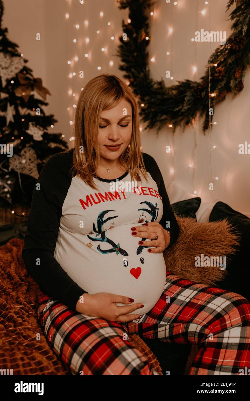 Schwangere Frau sitzt im Schlafanzug mit auf dem Bett im Schlafzimmer. Weihnachtsmorgen. Das Interieur des neuen Jahres. Valentinstag-Feier Stockfoto