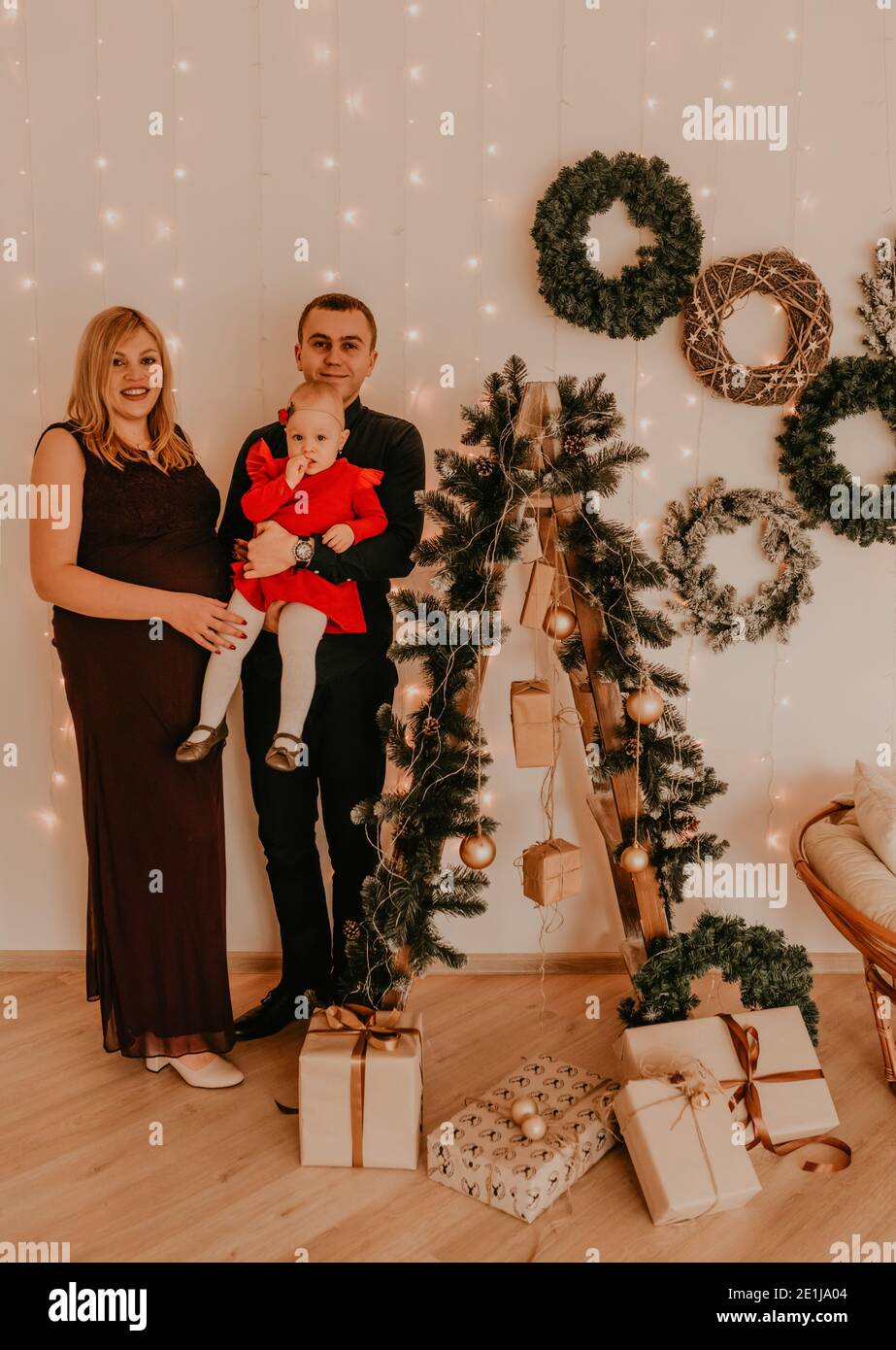 Glückliche Familie mit schwangerer Frau auf der Trittleiter schmückt das Haus für das neue Jahr. Weihnachtsmorgen. Innen. Valentinstag-Feier Stockfoto