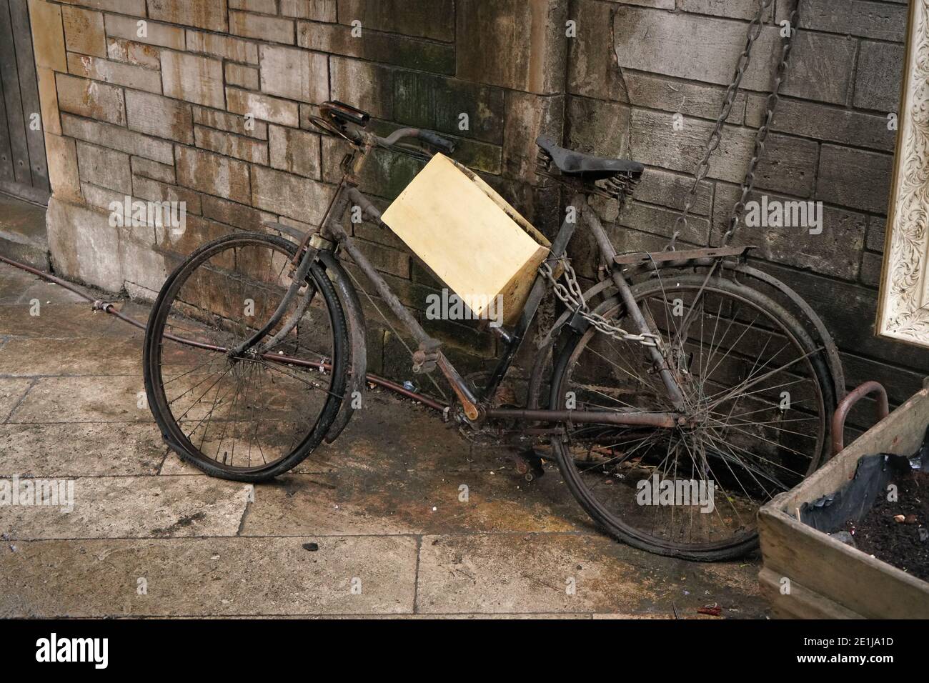 Ungenutztes rostig altes schwarzes Fahrrad mit Holzkiste in der Nähe geparkt Schmutzige Ziegelwand Stockfoto