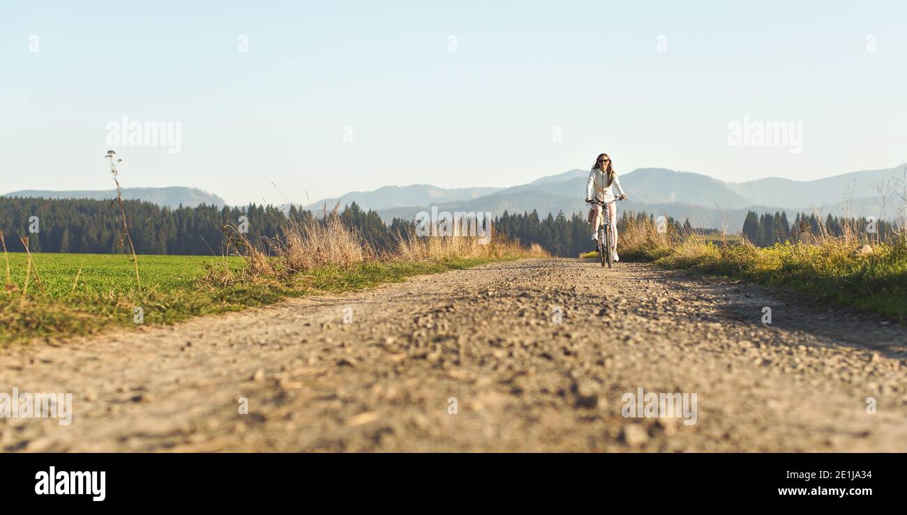 Junge Frau, die auf staubiger Straße im Freien Fahrrad fährt. Breites Foto mit Platz für Text Stockfoto