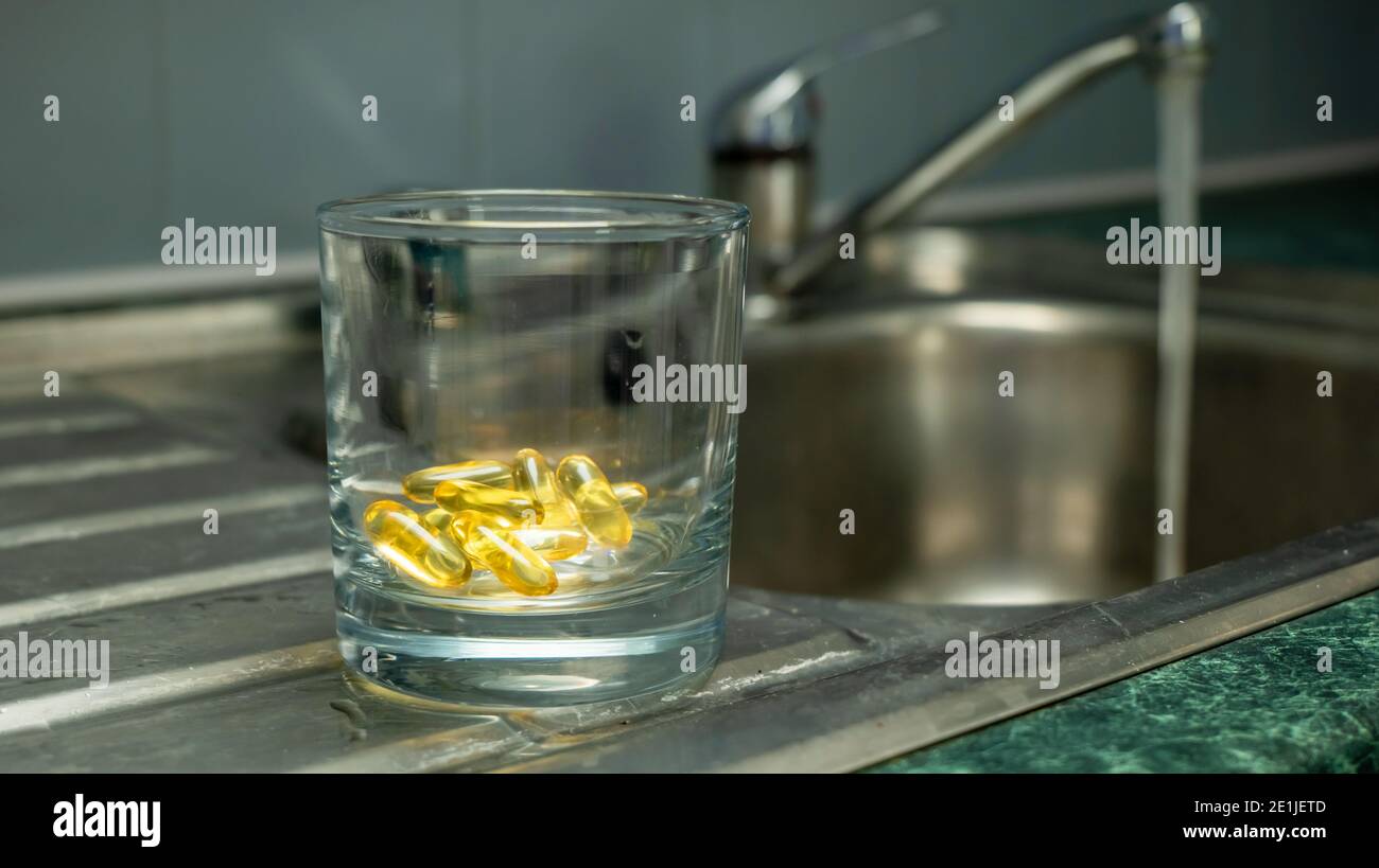 Ein Glas in der Hand gehalten mit gelb goldfarbenen Kapseln - Nahrungsergänzungsmittel, Vitamine, Medizin Stockfoto