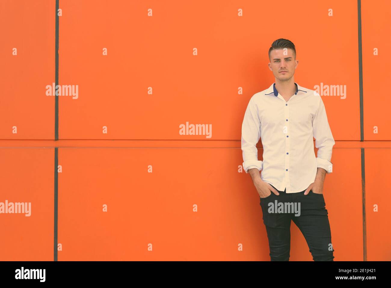 Jungen gutaussehenden Mann stehen und lehnte sich gegen orange Betonwand Stockfoto