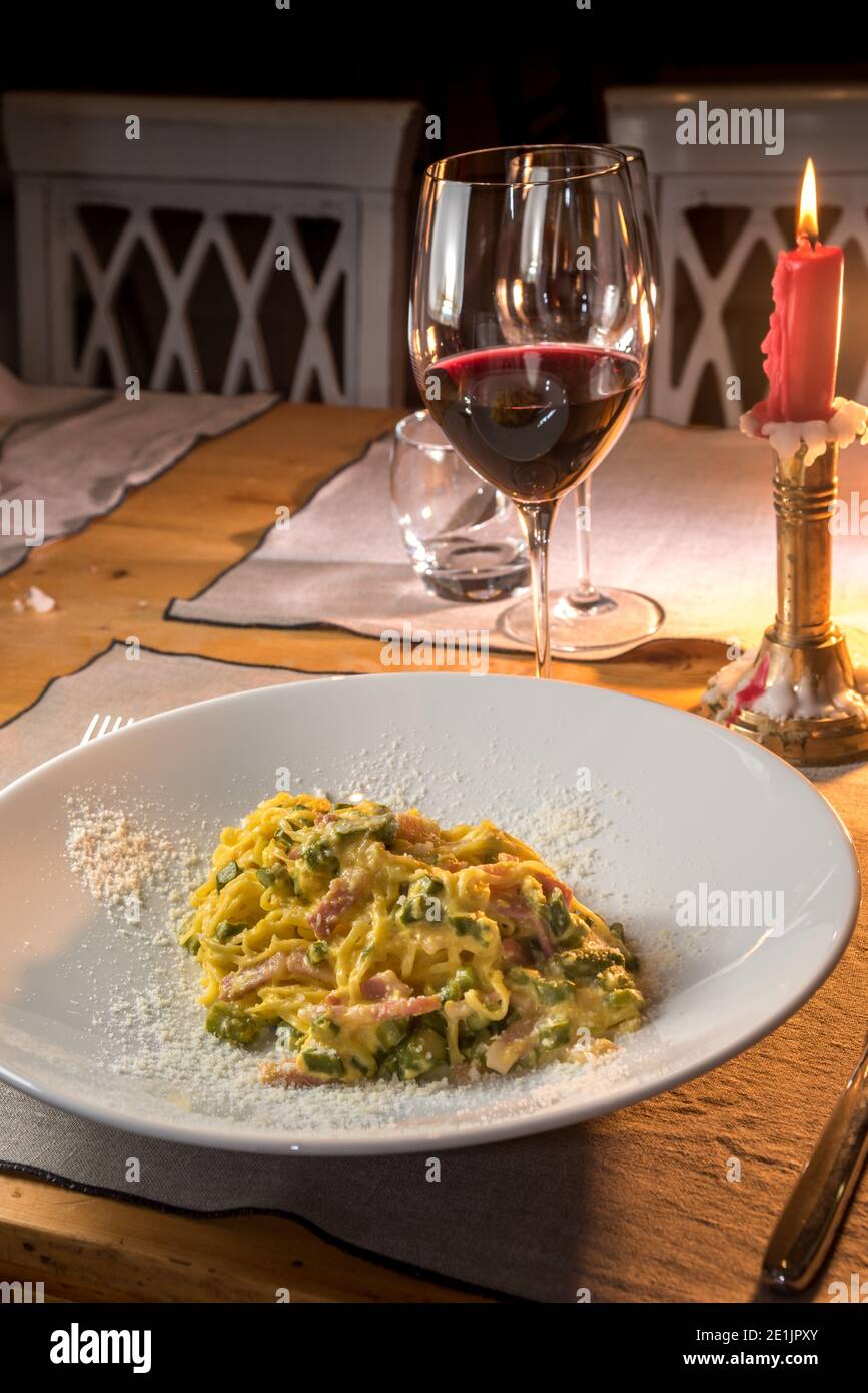 Carbonara Fettuccine mit Spargel. Eier Spaghetti mit Speck, Eier und Parmesan auf dem Trattoria-Tisch mit einem Glas Wein und Kerzenschein Stockfoto