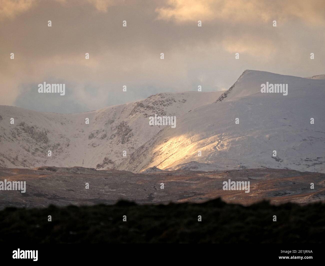 Dramatisches Abendlicht durch stürmische Wolken erhellt Schnee auf Kidsty Pike & High Street in Golden Hour Cumbrian Landschaft in England, Großbritannien Stockfoto