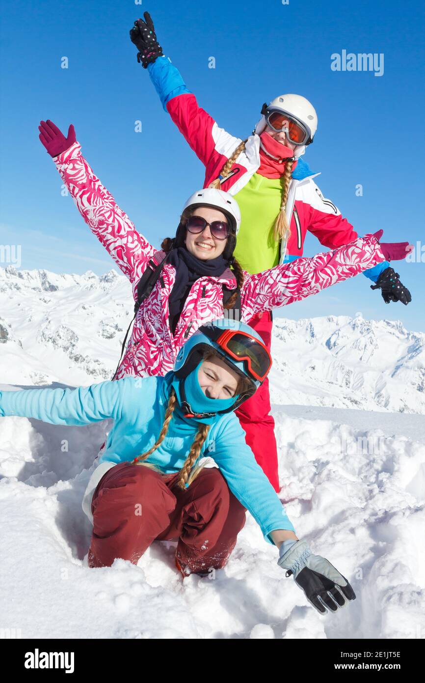 Glücklicher Familienurlaub im Winter. Drei Mädchen mit sehr bunten Kleidern posieren im frischen Schnee und blauen Himmel und heben ihre Hände Stockfoto