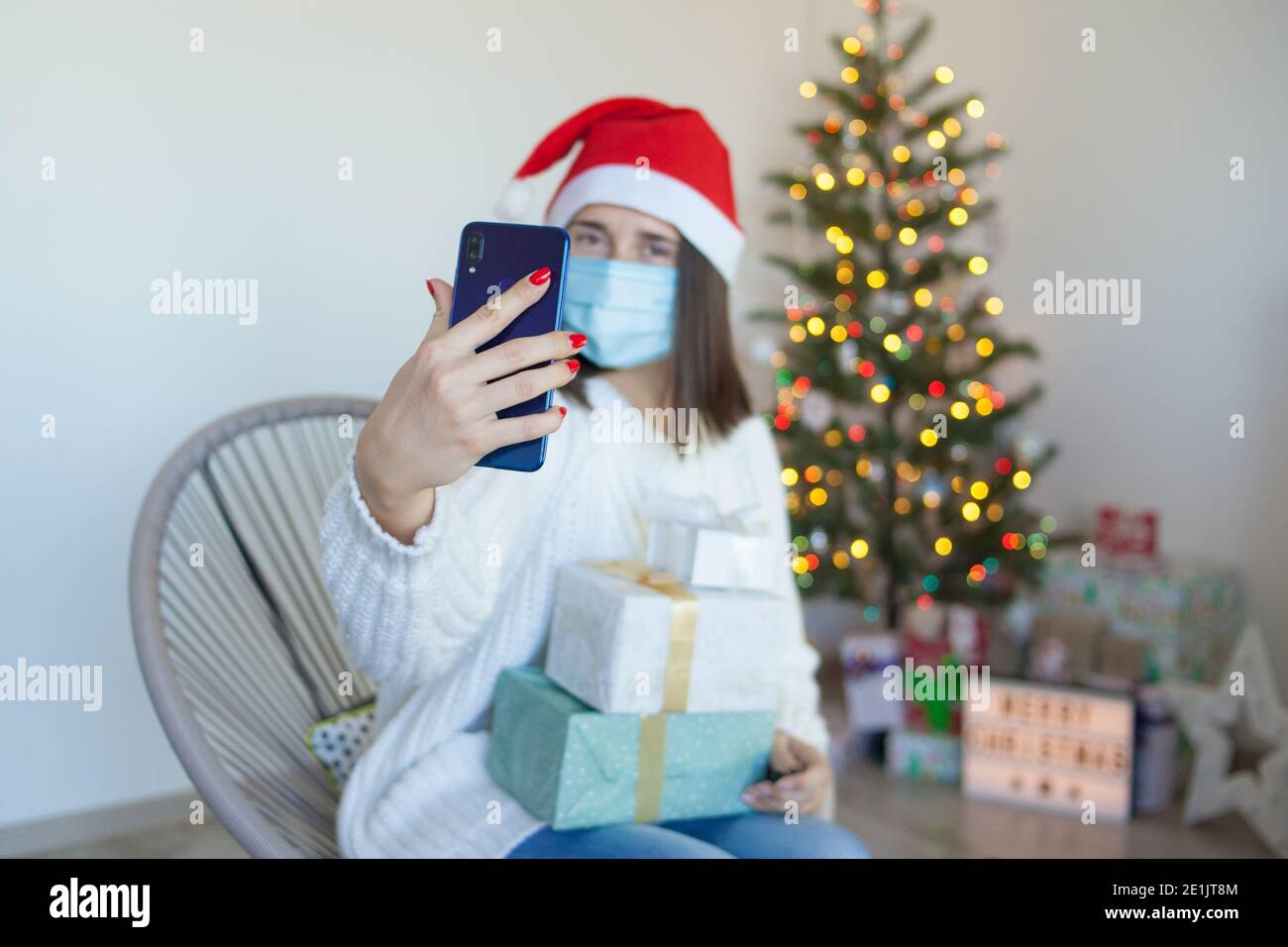 Frau in medizinische Maske mit Geschenkboxen mit einem Video Rufen Sie am Telefon an Stockfoto