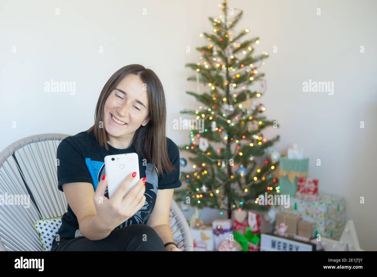 Frau mit einem Videoanruf am Telefon in der Nähe von weihnachtsbaum Stockfoto