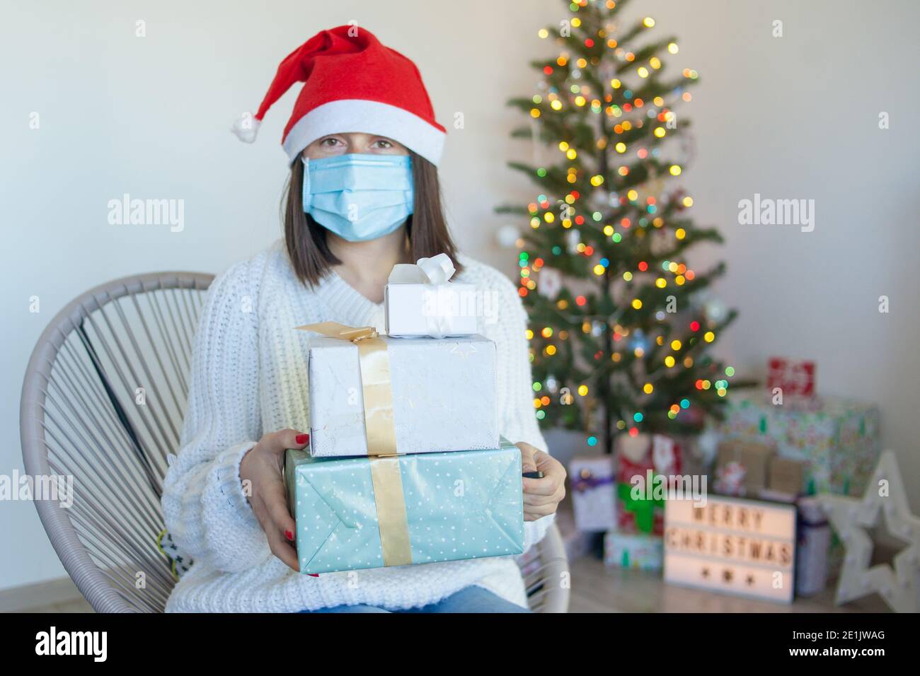 Frau in medizinische Maske mit Geschenkboxen in der Nähe von weihnachtsbaum Stockfoto