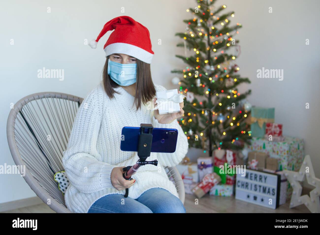 Frau in medizinische Maske mit Geschenkbox mit einem Video Rufen Sie am Telefon an Stockfoto