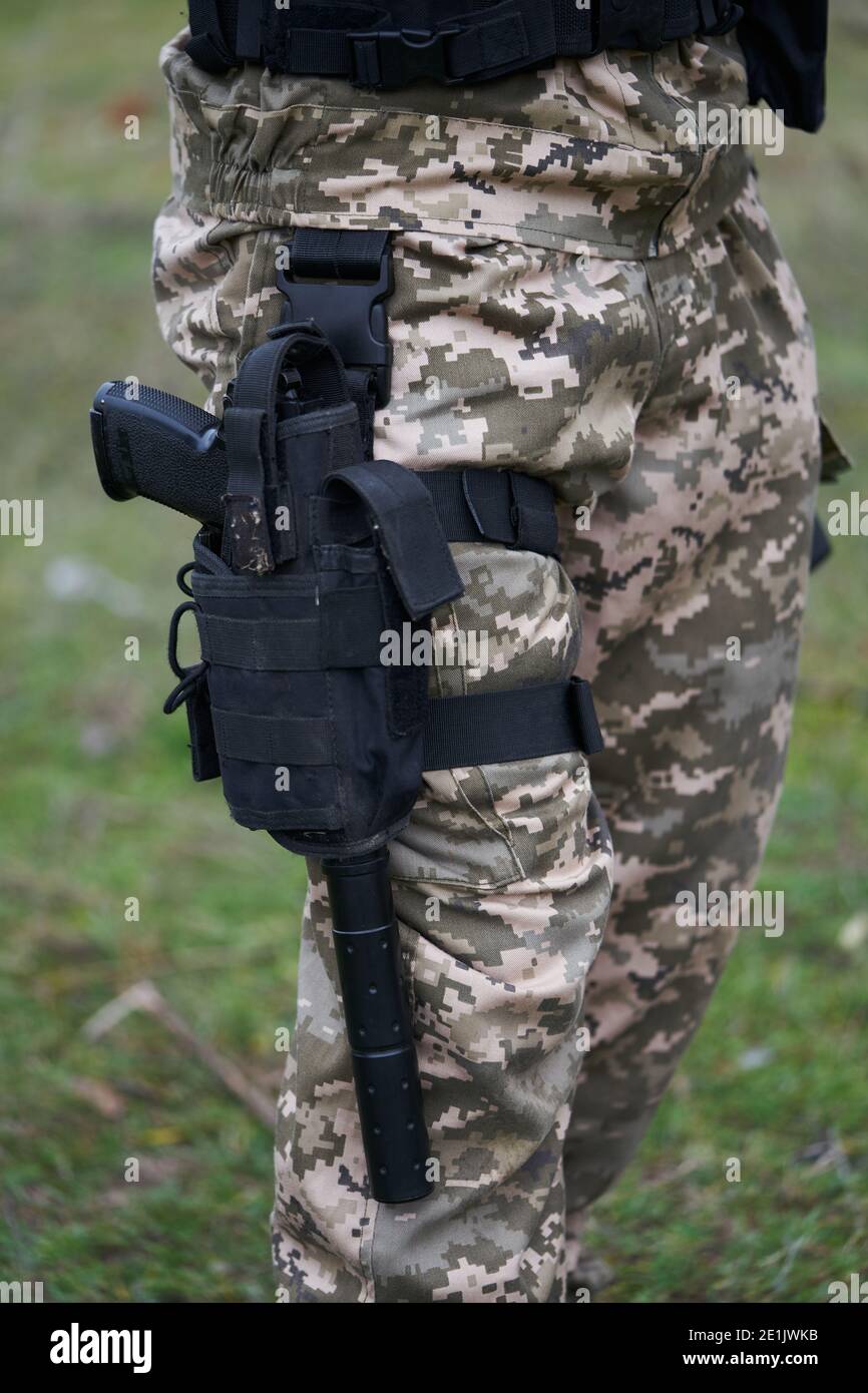 Nahaufnahme einer Pistole mit einem Schalldämpfer in einem Holster Auf dem Bein eines Soldaten in Tarnuniform Stockfoto