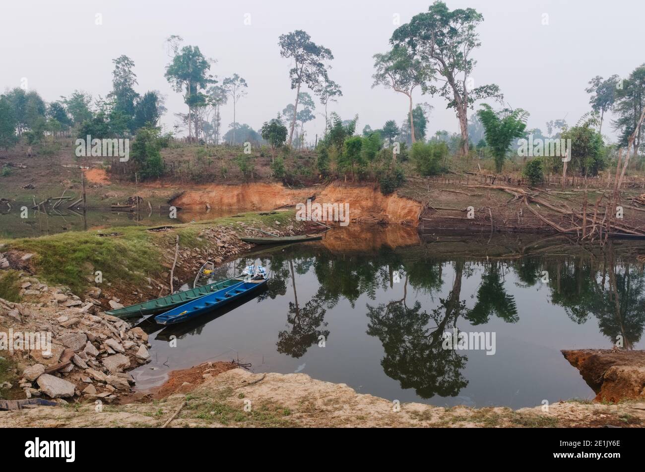 Hölzerne Fischerboote in der kleinen Bucht des Nam Theun Flusses. Traditionelle ländliche Ansicht des kleinen Dorfes in der Nähe des Flusses in Laos. Bäume spiegeln sich im Wasser. Thalang, Stockfoto