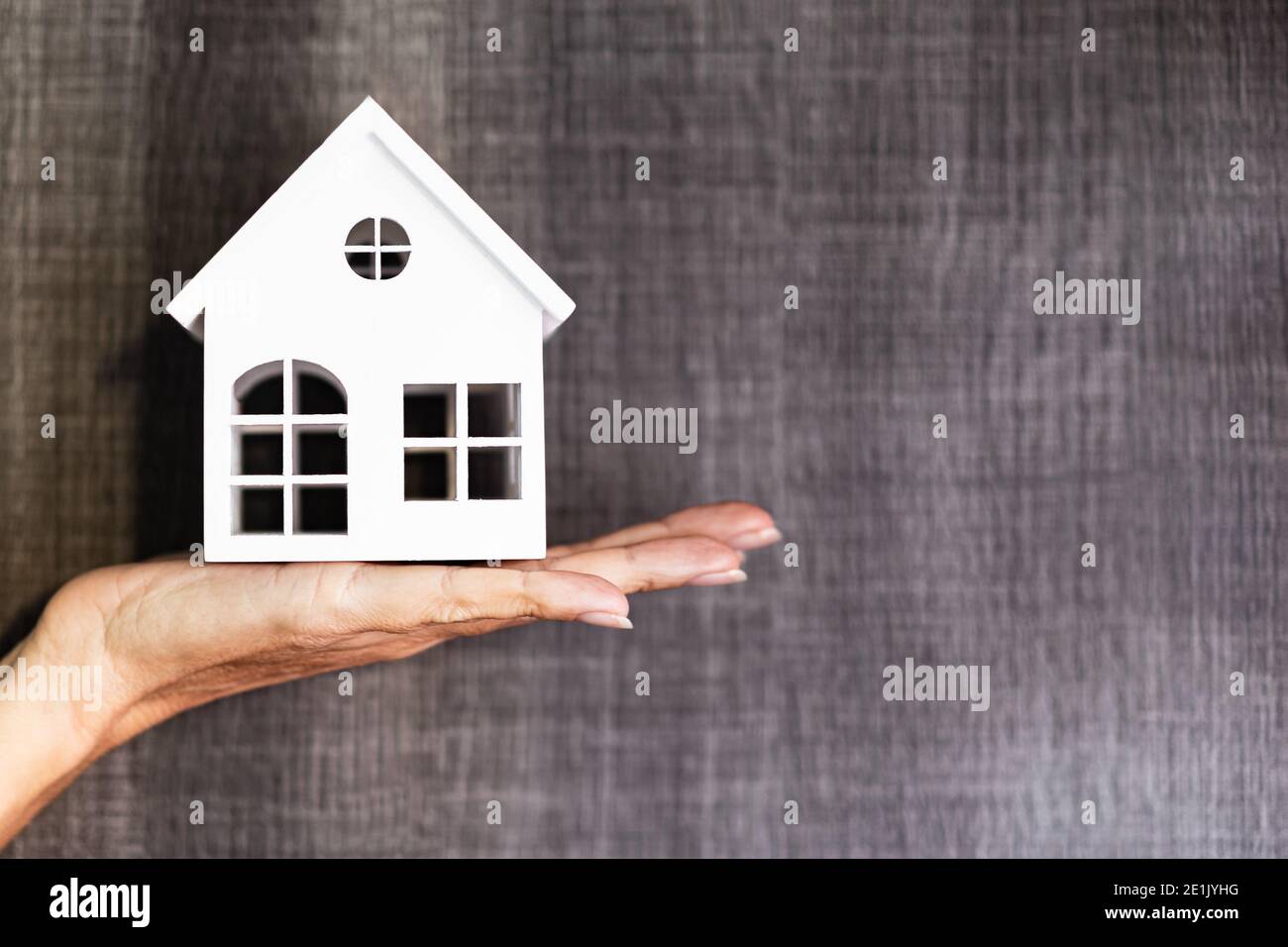 Hand hält ein Haus Modell. Immobilienmakler bieten Haus, Sachversicherung und Sicherheit. Kauf und Miete Haus Konzept. Grauer Hintergrund. Stockfoto