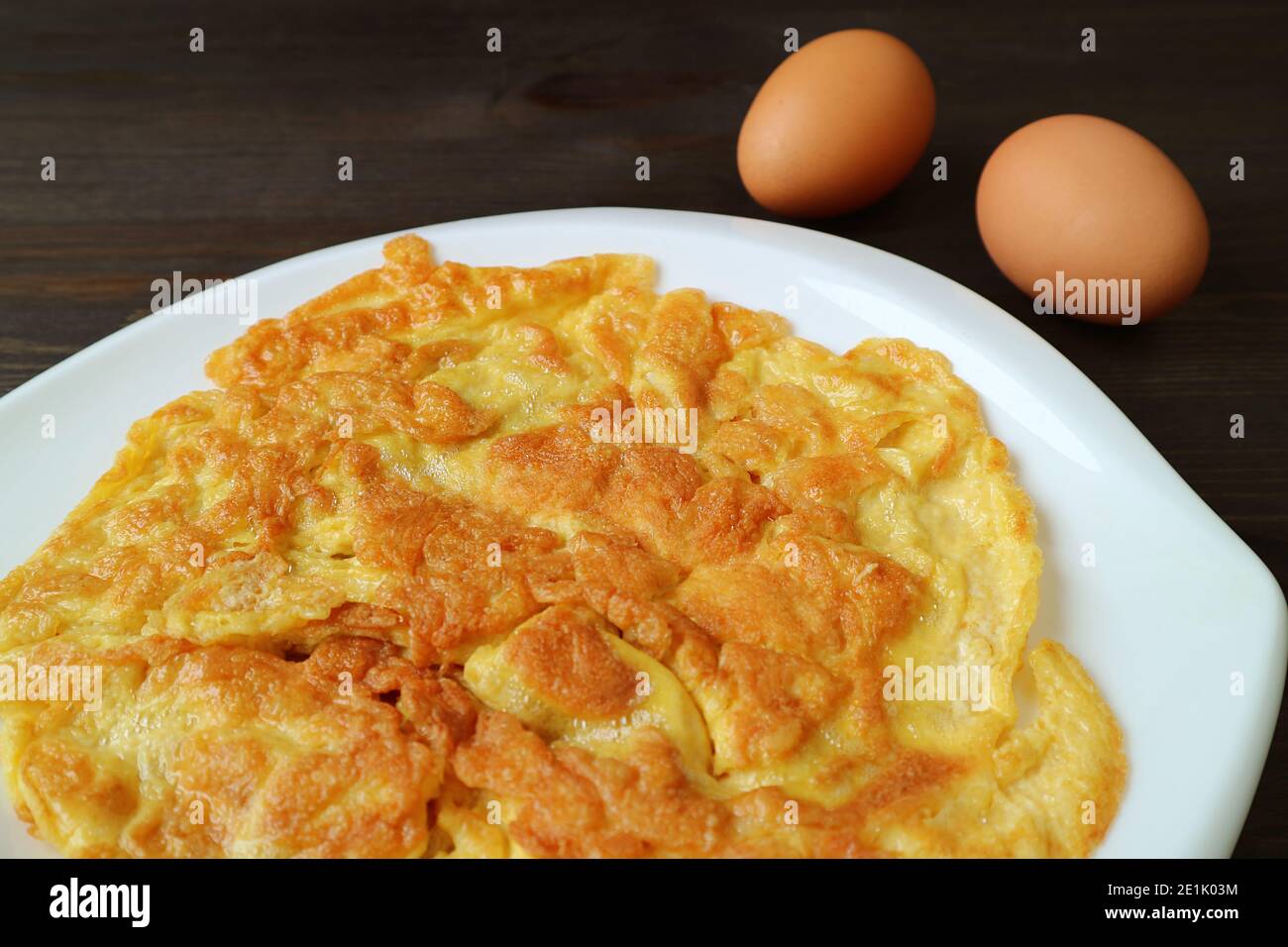 Teller mit thailändischem Omelett mit zwei rohen Eiern auf Dunkelbrauner Holztisch Stockfoto