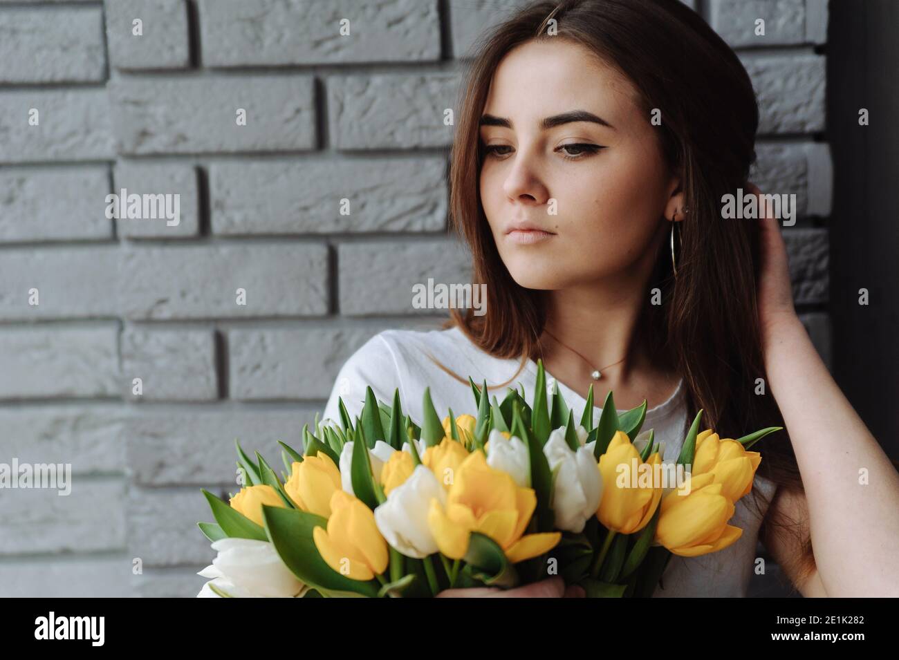 Mädchen mit Blumenstrauß auf dem grauen Hintergrund mit dem Platz für Ihren Text. Mädchen mit Tulpen. Internationaler Frauentag Stockfoto