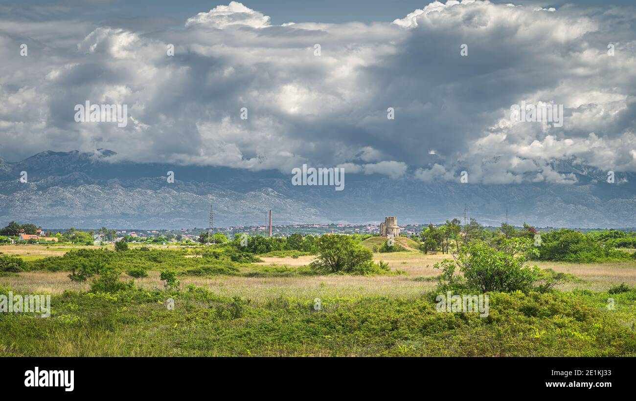 Sandstein St. Nikolaus Kirche mit Dinarischen Alpen im Hintergrund, ist römisch-katholische Kirche zwischen Zaton und Nin in Kroatien Stockfoto