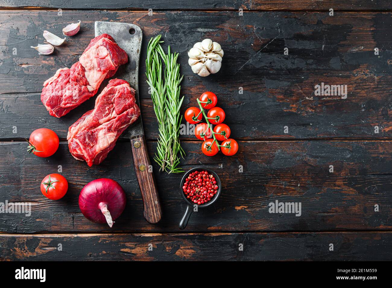 Bio rohes Chuck Eye Roll Beef Steak geschnitten mit Rosmarin roten onin, Knoblauch Pfefferkörner und Tomaten auf alten dunklen Holztisch. Draufsicht mit Platz für te Stockfoto