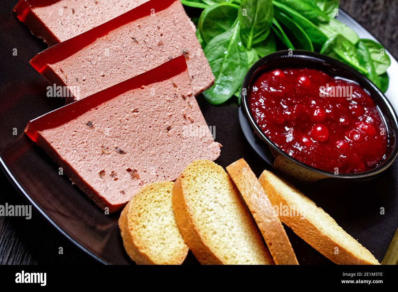 Französisches Gericht Entenleber Pastete mit Cranberry Marmelade auf einem schwarzen Teller serviert mit Cranberry-Sauce, Spinat und Brioche Croutons, mit goldenem c Stockfoto