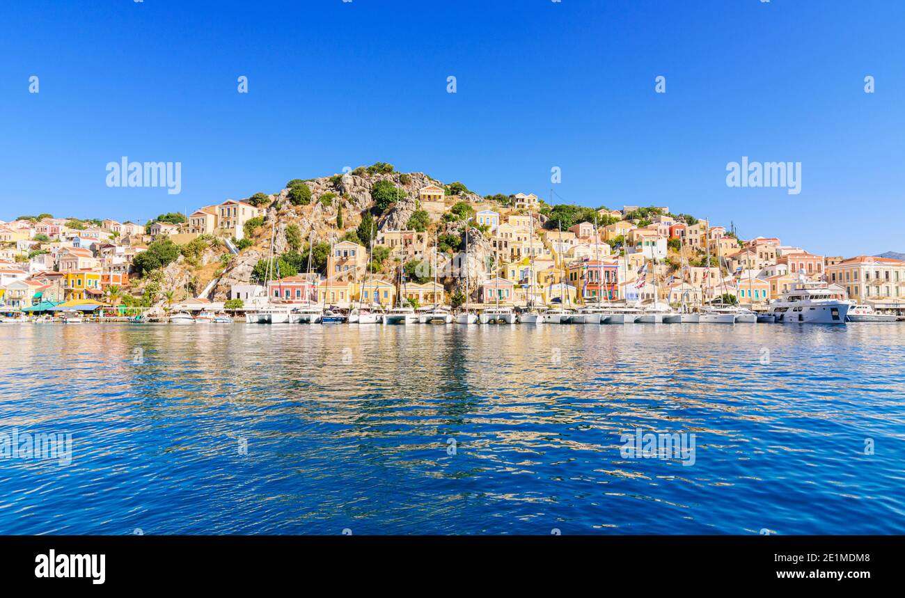 Symi, Griechenland, die neoklassizistischen Villen blicken auf Boote, die am malerischen Hafen von Gialos Town, Symi Island, Dodekanes, Griechenland, festgemacht sind Stockfoto