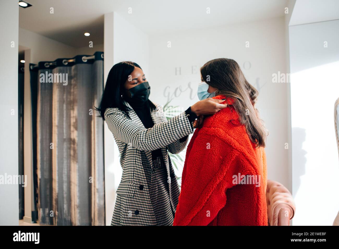 Modegeschäft Arbeiter hilft einer Kundin beim Versuch auf Kleidung. Zwei Frauen tragen eine schützende Gesichtsmaske in einem Geschäft. Neues normales Konzept Stockfoto