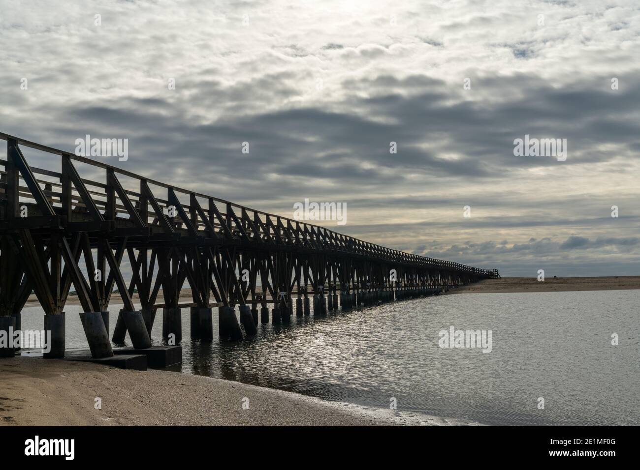 Ein langer hölzerner Steg Pier führt von einem Strand zu Ein weiterer über einem kleinen Meeresarm Stockfoto