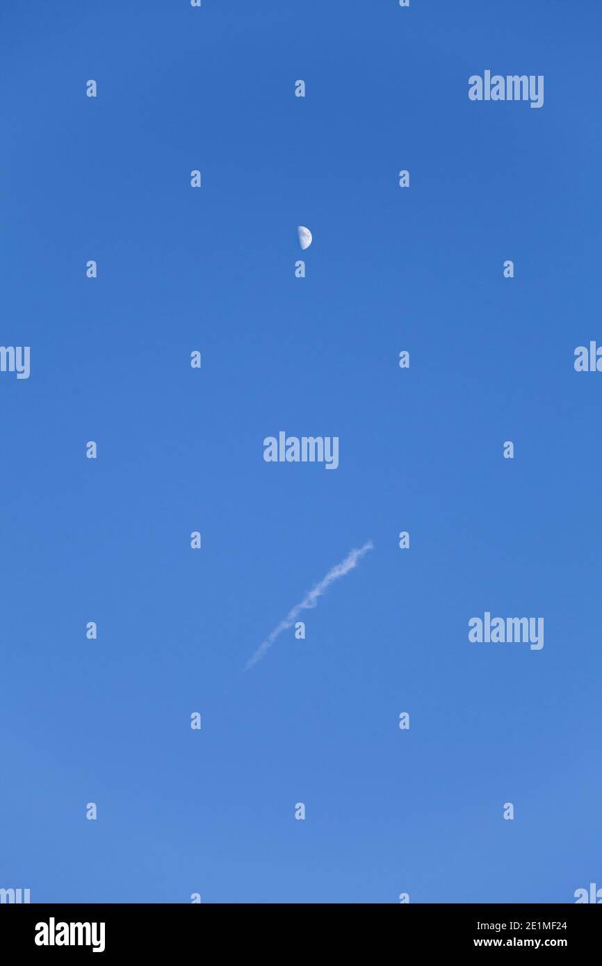 Eine vertikale Aufnahme des Mondes aus tiefem Winkel Der Himmel während des Tages mit einem Flugzeug contrail Stockfoto