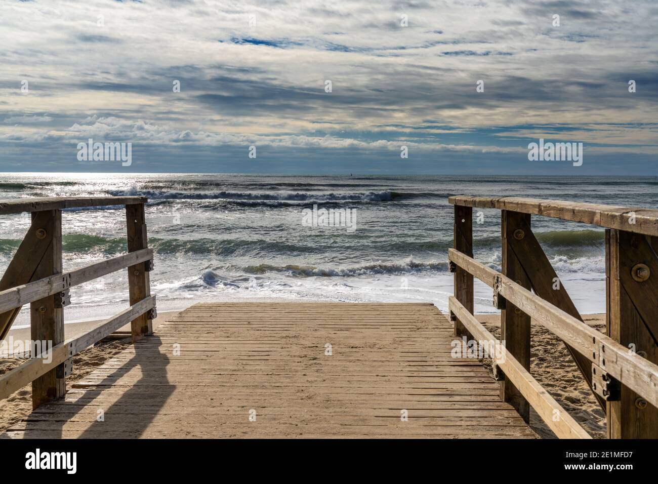 Eine Holzpromenade und Zugang zum Strand führt direkt zum Strand Mit stürmischen Wellen und Himmel Stockfoto