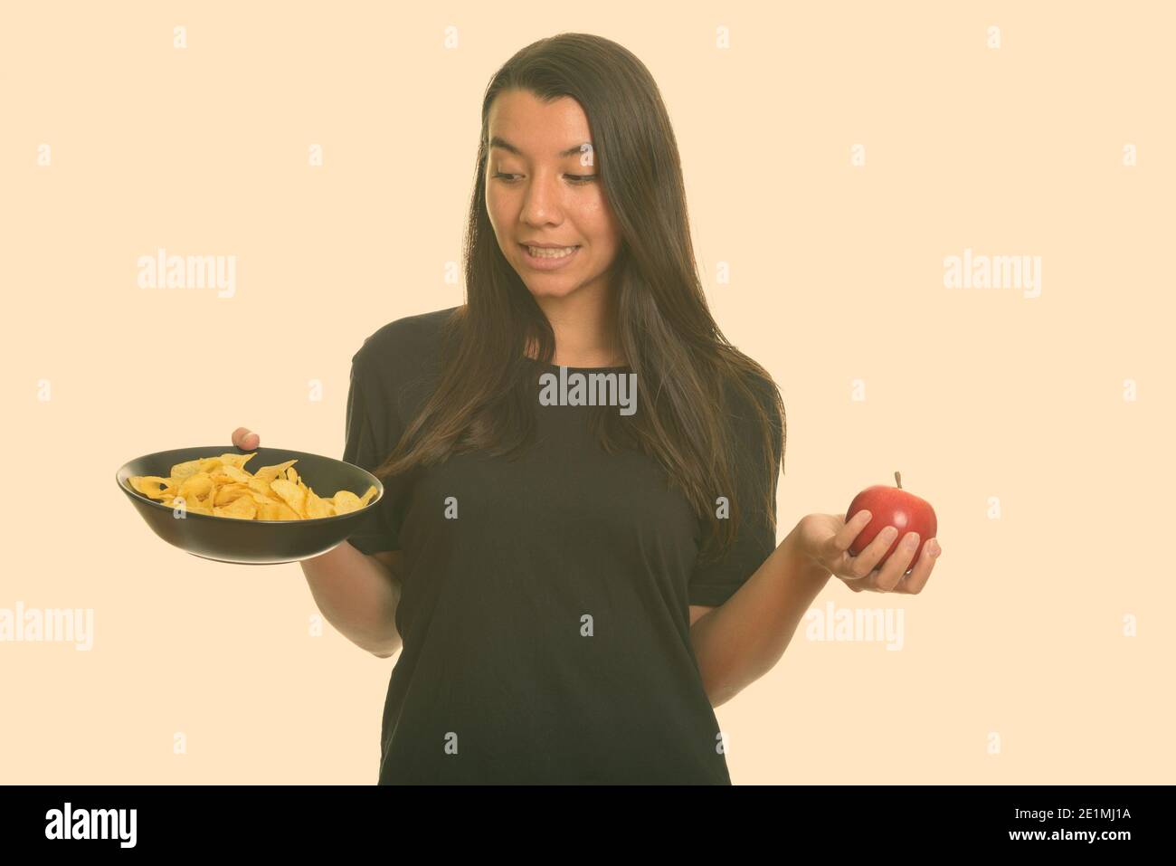 Junge kaukasische Frau Wahl zwischen Schüssel Kartoffelchips und Roter Apfel Stockfoto