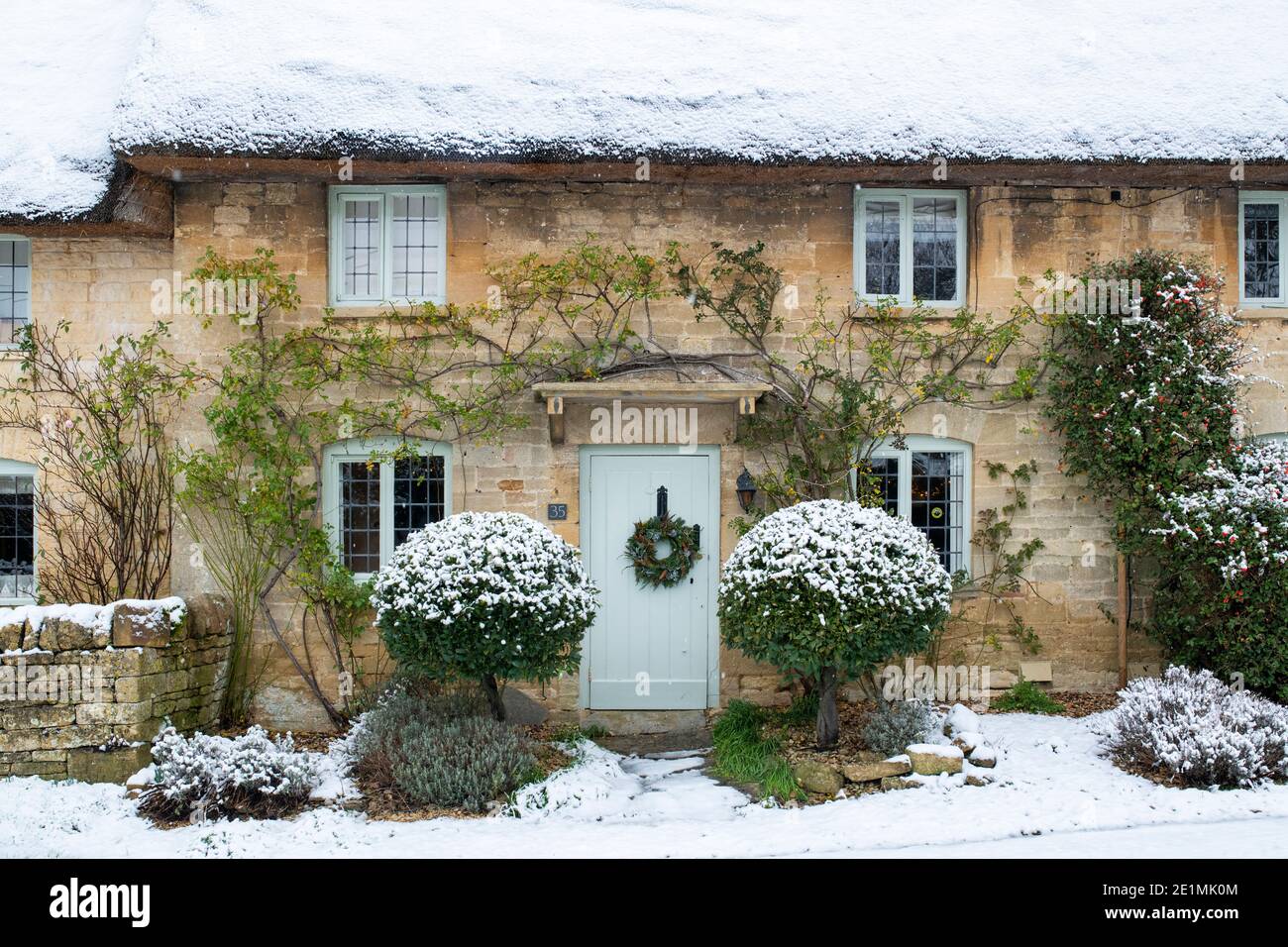 Cotswold Stein Reetgedeckten Hütte mit weihnachtskranz im Dezember Schnee. Taynton, Cotswolds, Oxfordshire, England Stockfoto