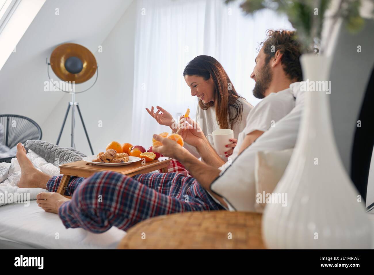 Ein junges Paar, das Spaß hat, während es leckeres Essen für ein Frühstück im Bett in ihrem Schlafzimmer isst. Liebe, Beziehung, zusammen Stockfoto