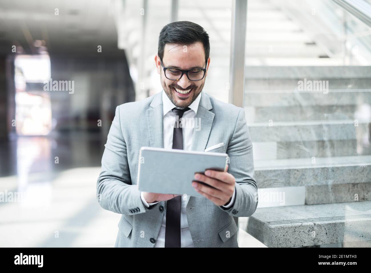 Porträt des Geschäftsmannes lächelnd und mit Tablet für die Arbeit, während auf dem Glas lehnend. Im Hintergrund Treppe. Stockfoto