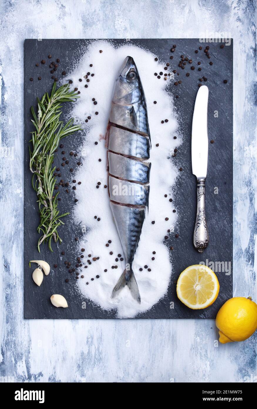 Flatlay von Scheiben frischen Fisch auf einem Schieferstein Textur Teller mit Rosmarin, Knoblauch, Zitronenscheiben, Salz und Messer dekoriert. Food Hintergrund mit Platz Stockfoto